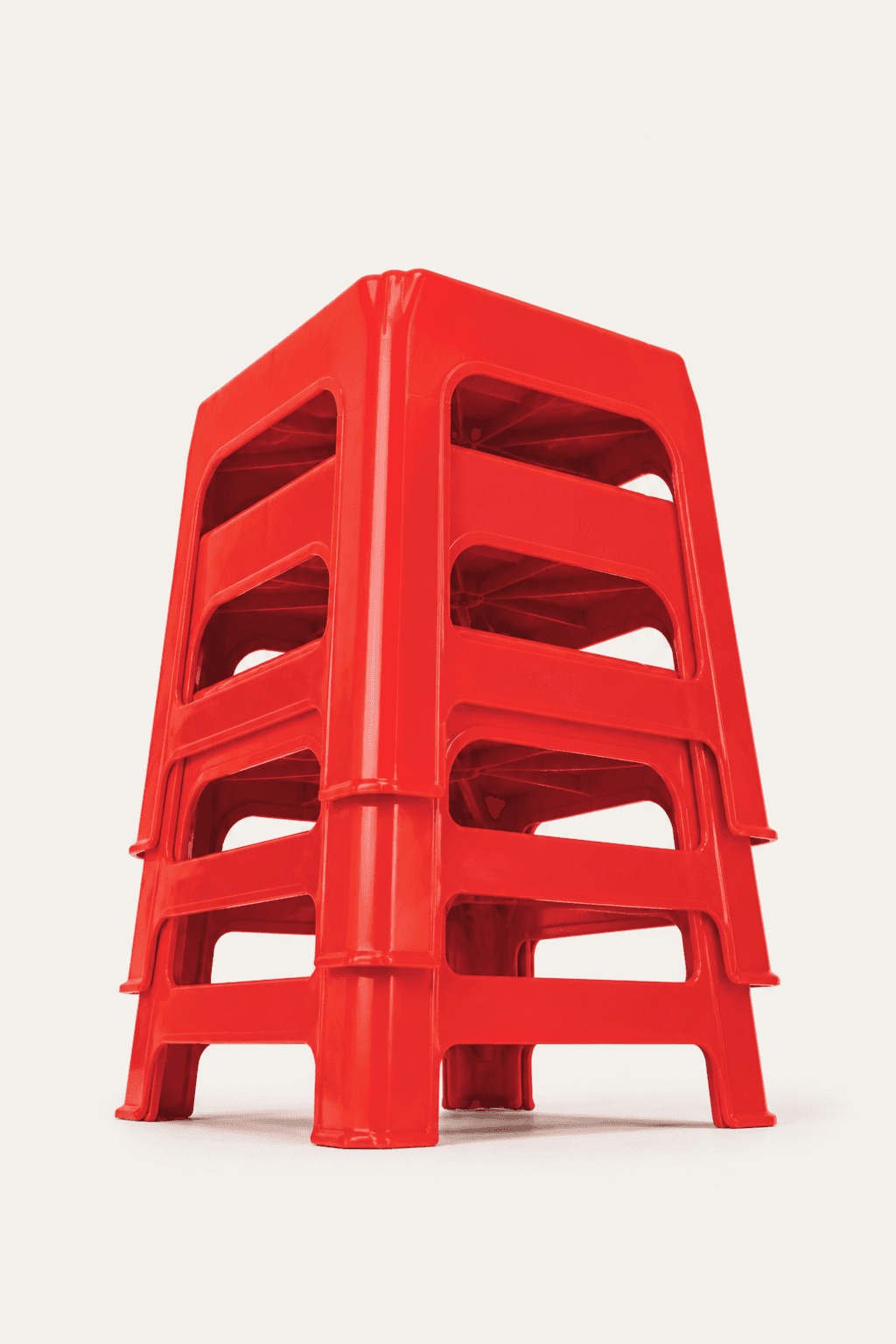 Stack of Vietnamese red plastic stools seen from below on a warm off-white background